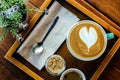 Coffee cup with heart shape latte art in wooden tray with brown sugar, spoon, tea, napkin, and decorating flower Royalty Free Stock Photo