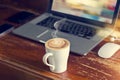 Coffee cup with laptop, mouse and earphone on old wooden table