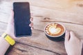 Coffee cup with latte art heart pattern on a wooden table background and Young woman hand holding smartphone Royalty Free Stock Photo