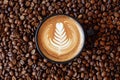 Coffee cup with latte art surrounded with coffee beans top view. Cup of freshly brewed cappuccino closeup on roasted coffee beans Royalty Free Stock Photo