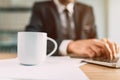 Coffee cup mockup image, blank white mug on office desk with businessman working on laptop computer Royalty Free Stock Photo