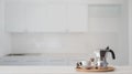 Coffee cup and Moka pot in wooden tray on white counter with blurred kitchen background Royalty Free Stock Photo