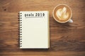 Coffee cup and notebook with goals 2019 on rustic desk