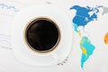 Coffee cup over world map and financial documents - view from top