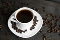 Coffee cup with roasted coffee beans on wooden table background. Mug of black coffe with scattered coffee beans on a