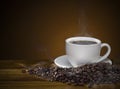 Coffee cup with roasted brown coffee beans and smoke on wooden t