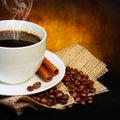 Coffee cup with saucer and coffee beans on burlap over dark Royalty Free Stock Photo