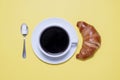 Coffee cup and saucer with croissant and spoon on yellow Royalty Free Stock Photo
