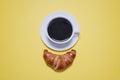 Coffee cup and saucer with a croissant on yellow