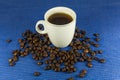 Coffee cup and saucer on rough cotton table. Dark blue background. Close up dark roasted fair trade coffee beans