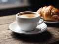 coffee cup and saucer sit on a wooden table next to a croissant