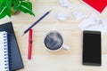 Coffee cup with smartphone, crumpled paper, glasses, notebooks, pen, pencil, paper clips, green leaves pot on vintage wooden table Royalty Free Stock Photo