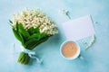 Morning breakfast concept. Coffee cup with spring bouquet of flowers lily of the valley and empty greeting card top view.