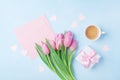 Coffee cup, spring tulip flowers, gift box and pink paper card on blue pastel table top view. Greeting for Womans or Mothers Day.