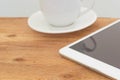 Coffee cup with tablet with blank black screen on wooden table