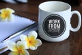 Coffee cup with text - work from home, with Bali frangipani flowers, pen and notebook on desk. Social distancing issues concept.