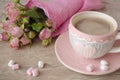 Coffee cup on a wooden table with bouquet of pink roses. Knitted heart shaped cup