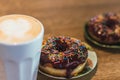 Coffee with a drawn heart and milk on a wooden table in a coffee shop. two chocolate donuts with scattering on the table Royalty Free Stock Photo