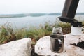 Coffee drops from aeropress on metal mug on cliff at lake, brewing alternative coffee at camping. Making hot drink at picnic