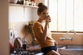 Coffee-fuelled morning thoughts. A young woman casually drinking coffee while standing in her kitchen. Royalty Free Stock Photo