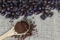 Coffee grind in wooden spoon on sackcloth with coffee beans background. Copy space.