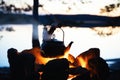 Coffee in a kettle on campfire in forest on shore of lake at evening. Travel and camping concept.