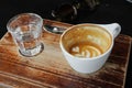 Coffee with latte art is drunk. Ceramic cup and glass of water on brown wooden table in cafe Royalty Free Stock Photo