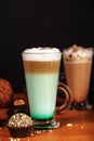 Coffee latte macchiato with mint syrup and whipped cream, in high transparent glasses with cakes, on a dark background Royalty Free Stock Photo