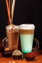 Coffee latte macchiato with mint syrup and whipped cream, in high transparent glasses with cakes, on a dark background Royalty Free Stock Photo