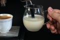 Coffee machine On the grate is a white cup of cafe. Barista holds creamer in his hand, whips milk Royalty Free Stock Photo