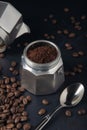 Coffee maker with ground coffee, coffee beans and metal spoon on dark textured background Royalty Free Stock Photo