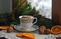 Coffee with marshmallow, walnut cones, and Christmas tree branches on an old wooden snowy window. Christmas and New Year