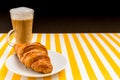 Coffee with milk in the Irish Cup next to the croissant on a white saucer on a striped table and copyspace.