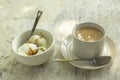 Coffee with milk and ice cream balls in white cups with spoons on a marble table surface close up
