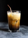 Coffee with milk and ice in a tumbler glass cup with a metal straw on a dark background