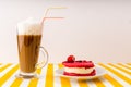 Coffee with milk in an Irish glass next to a raspberry cake on a yellow-and-white striped table. Royalty Free Stock Photo