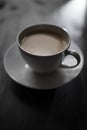 Coffee with milk in a white cup and saucer on a black wooden table, break for hot drinks front view Royalty Free Stock Photo