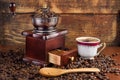 Coffee mill grinder and cup of coffee and wooden spoon on old retro background with roasted beans Royalty Free Stock Photo
