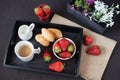 Coffee, mini French pastries and strawberries on wooden tray over black table. White and purple flowers in a decorative wooden Royalty Free Stock Photo