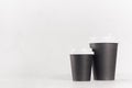 Coffee mockup - big and small blank black paper cups with white cap on white wood table with copy space, coffee shop interior. Royalty Free Stock Photo