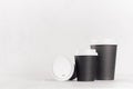 Coffee mockup - different size black paper cups and blank white cap on white wood table with copy space, coffee shop interior.