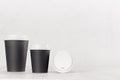 Coffee mockup - different size black paper cups and blank white cap on white wood table with copy space, coffee shop interior.