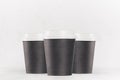 Coffee mockup - group of three blank black paper cups with white cap closeup on white wood table, coffee shop interior. Royalty Free Stock Photo