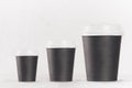 Coffee mockup - set of three different size blank black paper cups with white cap on white wood table, coffee shop interior. Royalty Free Stock Photo