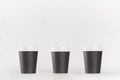 Coffee mockup - set of three small blank black paper cups with white cap on white wood table, coffee shop interior. Royalty Free Stock Photo