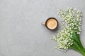 Coffee mug with bouquet of flowers lily of the valley on gray stone table top view in flat lay and minimalistic style. Royalty Free Stock Photo