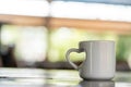 A coffee mug with a love shaped handle standing on the top of a table with blurred out bright background