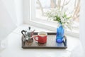 Coffee mug, metal coffee maker, flowers on wooden tray on sill Royalty Free Stock Photo
