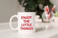 Coffee mug with text ENJOY THE LITTLE THINGS in workplace background Royalty Free Stock Photo