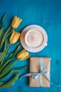 Coffee mug with yellow tulip flowers and present box on blue rustic table from above, breakfast on Mothers day or Womens Royalty Free Stock Photo